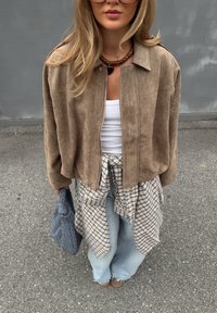 Brun mocka croppet jakke, hvit tanktop, rutete skjorte knyttet i livet, lyseblå vide jeans, grå vevd bag og brune sko.
