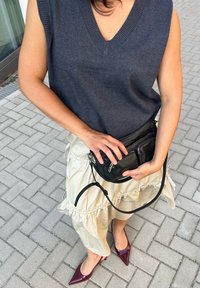 Bezrękawnik w ciemnoszarym kolorze z dzianiny, kremowa spódnica midi z falbanami, czarna torebka na ramię oraz bordowe lakierowane czółenka z szpiczastym noskiem.