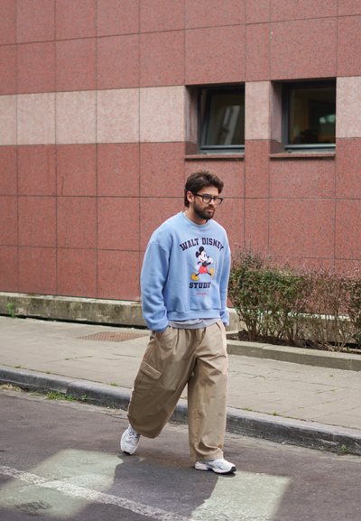 Sudadera azul claro con el texto "WALT DISNEY STUDIO" y gráfico de Mickey Mouse, combinada con pantalones de pierna ancha beige y zapatillas blancas.