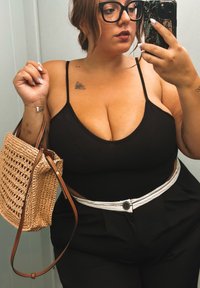Top nero senza maniche con spalline larghe e scollatura alta, abbinato a pantaloni a vita alta e una borsa di paglia color tan. Cintura bianca con fibbia circolare.