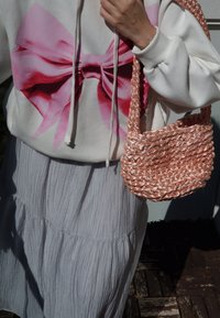 Bela kapuca s velikim roza mašnom na grafici, u kombinaciji sa teksturiranom sivom slojevitom suknjom i pletenom roza torbom.