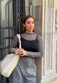 Langärmliges graues Oberteil, das über einem schwarzen Tanktop getragen wird, kombiniert mit grauen Hosen. Eine strukturierte beige Umhängetasche und mehrere Ringe akzentuieren den Look.