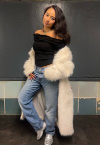 Svart avtoppa med skulderåpning, lyseblå høy midje jeans og hvit pelskåpe. Sølvfargede sneakers med tekstur. Minimal smykker.