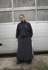 Schwarze Zip-Up Sweatshirt mit lockerer Passform, kombiniert mit einem langen schwarzen Rock mit Seitestreifen und schwarzen Schuhen mit strukturierten Sohlen.