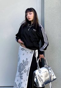 Sort lynlåsjakke med hvide striber, blomstret hvid nederdel og skinnende sølvhåndtaske. Tilbehør inkluderer en kædenekke og ringe.