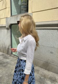 Λευκό πουκάμισο με μακριά μανίκια και κουμπιά, διακοσμημένο με δαντέλα, συνδυασμένο με φλοράλ μπλε φούστα, η οποία έχει σκούρα λουλούδια και ρέουσα σιλουέτα.