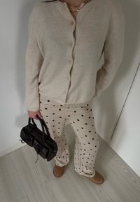 Cardigan beige en tricot avec boutons, pantalon beige à pois marron foncé, et petit sac à main marron foncé. Style cosy avec textures douces.
