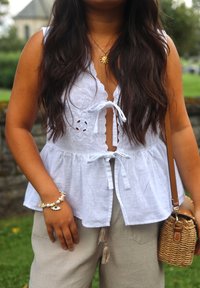 Valge linane ülemus, millel on tikitud lillemotiivid, sidumisrihm ja kõverad ääred. Koos heledate beežide pükste ja kootud kotiga.