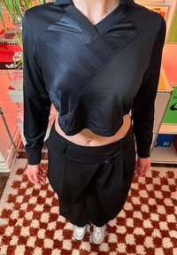 Haut noir court à manches longues avec un design texturé et un col en V, associé à un pantalon noir ample avec une fermeture à bouton.