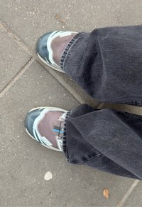 Chaussures de sport avec dessus en mesh gris et accents turquoise, bout arrondi et semelle en caoutchouc ; portées avec un jean foncé sur une surface pavée.