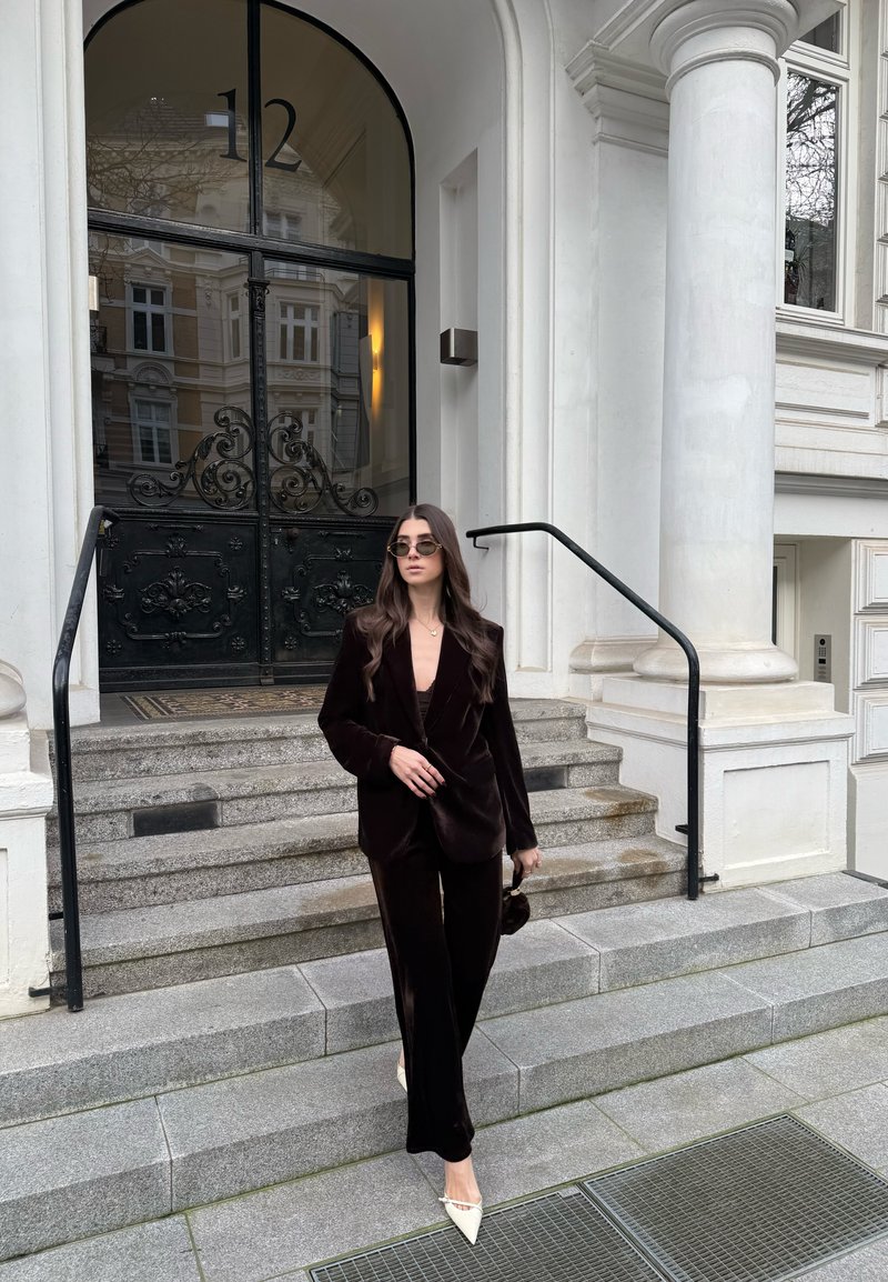 Donna in completo di velluto nero e tacchi bianchi che scende le scale di pietra fuori da un edificio con porta nera decorata al numero 12.