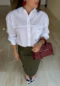 White button-up shirt, green leather pencil skirt, red handbag with a zipper, and black-and-white pointed-toe shoes. Red beaded earrings.