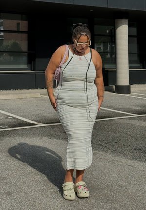 Vestido de punto blanco con rayas horizontales, forma ajustada y escote en forma de barco. Se lleva con zuecos de color claro que presentan decoraciones juguetonas.