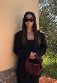 Svart överdimensionerad blazer, åtsittande svart topp och flätad burgundy handväska. Snygga solglasögon fulländar outfiten mot en naturlig bakgrund.