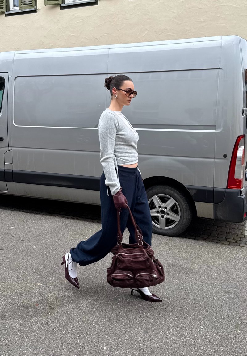 Szary krótkiego kroju sweter z dzianiny, granatowe luźne spodnie, bordowa torebka, białe skarpetki i bordowe szpilki na wysokim obcasie. Modelka idzie ulicą.