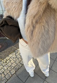 Lekki beżowy płaszcz z futrzaną imitacją, szary długi rękaw, brązowa pikowana torba i białe spodnie o szerokich nogawkach. Gładkie tekstury z casualowym obuwiem.