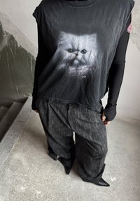 Čierne grafické tričko s motívom mačky a textom, kombinované s voľnými pruhovanými tmavými nohavicami a špicatými čiernymi topánkami. Textúrovaná tkanina.
