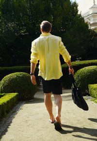 Kerge kollane lina särk, mustad lühikesed püksid ja sandaalid. Kandes musta kotti, kõndides mööda teed, mida ümbritseb tihe rohelus.