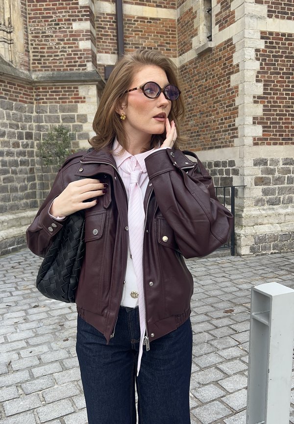 Vinröd skinnjacka med silverdetaljer, två framfickor, kombinerad med en vit skjorta och ljusrosa slips. Svart flätad handväska, mörka jeans.