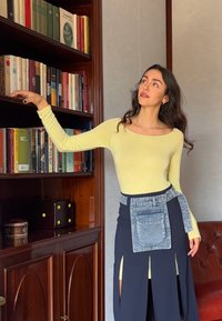 Blůza s dlouhým rukávem, přiléhavá, v bledě žluté barvě, spojená s sukní vysokého pasu v námořnické modré barvě, která má boční rozparky a denimový detail kapsy.