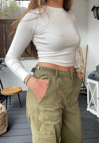 Λευκό μακρυμάνικο εφαρμοστό μπλουζάκι με λεία υφή, συνδυασμένο με ελαιοπράσινα cargo παντελόνια με μεγάλες τσέπες και ρυθμιζόμενη μέση.