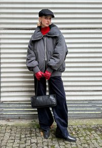 Giacca imbottita grigia oversize con colletto alto, top rosso, berretto nero, guanti rossi, borsa nera, pantaloni blu scuro e stivali neri robusti su uno sfondo testurizzato.