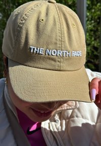 Khaki kapica za bejzbol iz bombaža z vezenim belim besedilom "THE NORTH FACE" spredaj. Ukrivljen rob, teksturirana površina in odprtinice za prezračevanje.