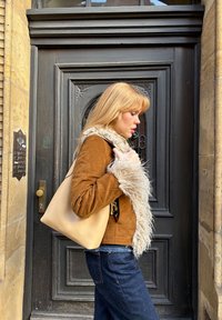 Brun ruskindsjakke med en fluffy beige krave, parret med blå denimbukser. En beige lædertotetaske bæres over skulderen.