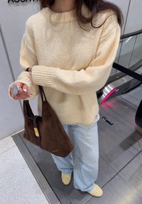 Helebeež kudumiga kõrge soonikkoega kaelusega kampsun, kombineeritud hele siniste laiade säärtega teksapükstega ja tumepruuni seemisnahast õlakotiga.