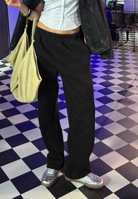 Schwarze Jogginghose mit elastischem Bund, kombiniert mit silbernen Sneakers und einer leicht beigen strukturierten Schultertasche. Weißes Button-Up-Hemd ist sichtbar.