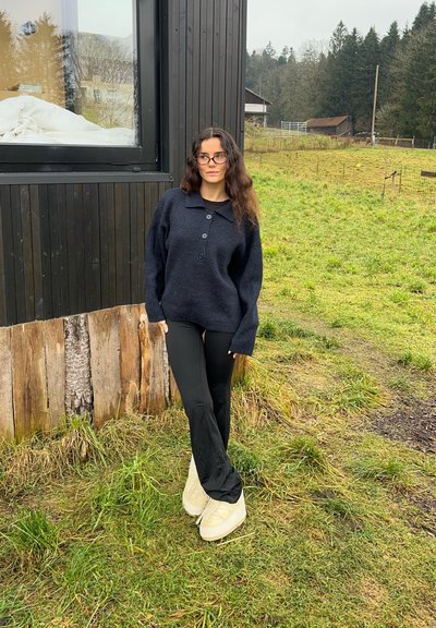 Suéter de gran tamaño en color navy con cuello tipo polo y tres botones, combinado con pantalones negros y zapatos de plataforma de color claro, frente a un fondo de hierba.