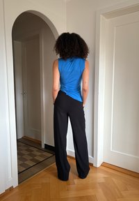 Haut sans manches bleu avec détail torsadé dans le dos et pantalon noir à jambes larges. Tissu lisse, encolure arrondie et design minimaliste.