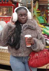Veste en fausse fourrure marron, jean bleu, cache-oreilles blancs, tenant un gobelet de café en papier. Sac à main rouge avec des accents dorés. Éléments de fond colorés.