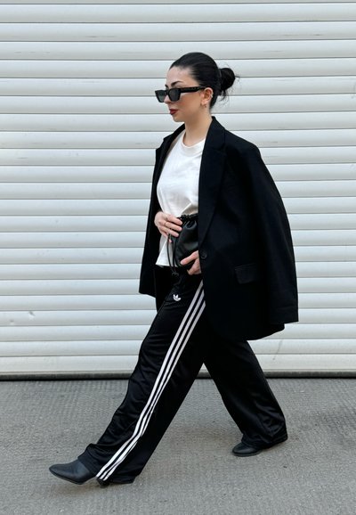 Blazer negro oversize, camiseta blanca y pantalones de chándal negros con rayas blancas. Botas de tacón negras y gafas de sol completan el atuendo.