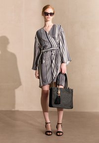 Zwart-wit gestreepte wikkeljurk met lange klokmouwen, gecombineerd met een zwarte tas met een geweven textuur en kleurrijke franje.