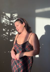 Vestito a quadri nero e rosso con sottili spalline, caratterizzato da una texture delicata. Sono visibili orecchini rotondi dorati e una fascia per capelli con motivo.