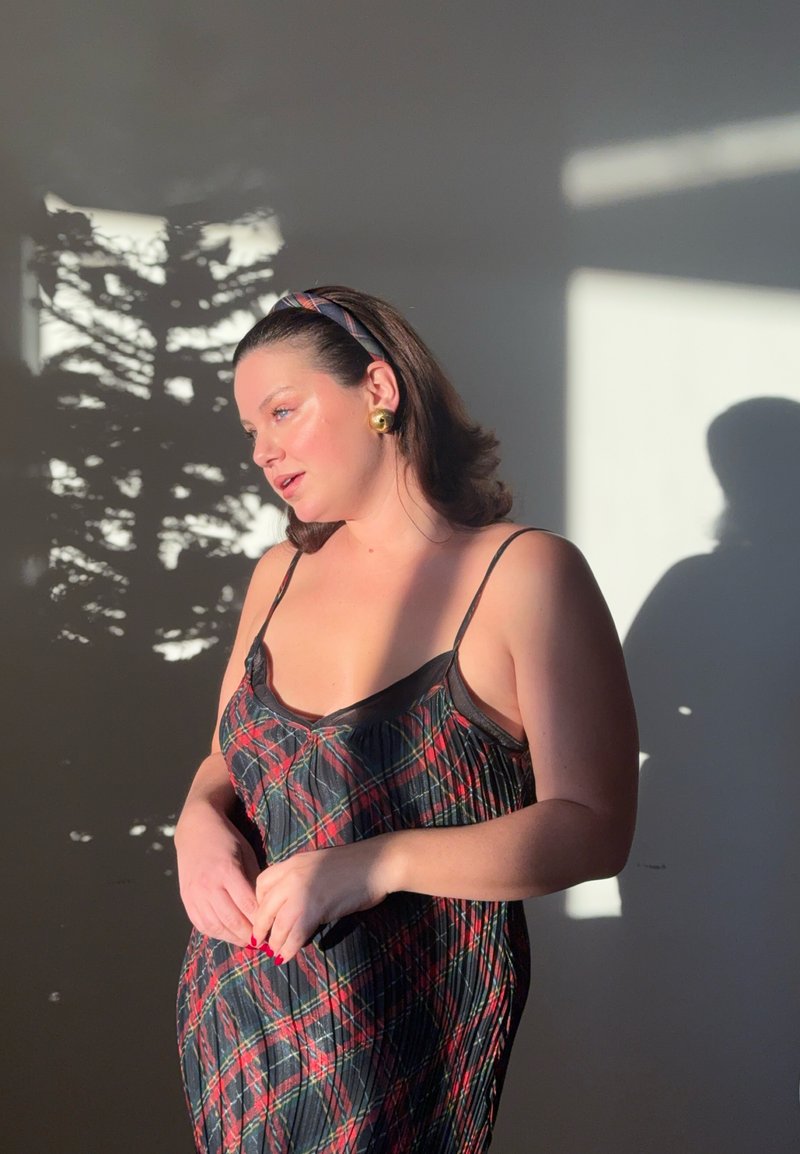 Robe à carreaux noirs et rouges avec fines bretelles, dotée d'une texture délicate. Des boucles d'oreilles rondes en or et un bandeau à motifs sont visibles.