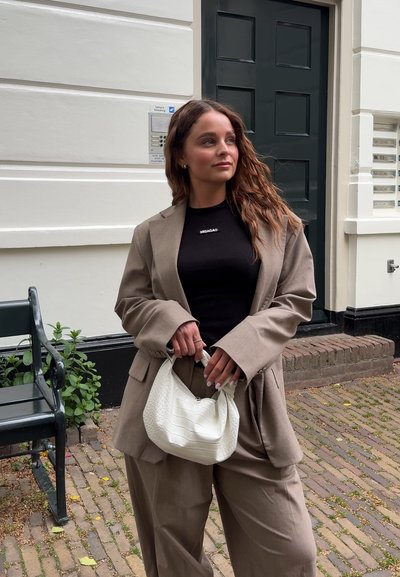 Blazer oversize beige y pantalones a juego, top negro ajustado, sosteniendo un bolso blanco texturizado. Iluminación suave y fondo urbano.