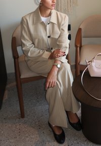 Costum șalbe cu dungi, croială lejeră, cu o jachetă cu nasturi și pantaloni largi. Pantofi negri și o geantă roz deschis pe o masă din lemn.