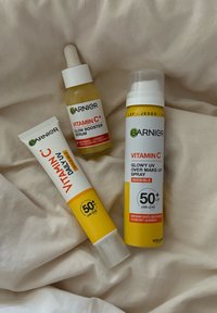 Tre prodotti per la cura della pelle Garnier: una bottiglia di siero giallo con pipetta, un tubo di crema bianca e una bottiglia spray con un cappuccio giallo, tutti etichettati con vitamina C.