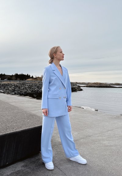 Blazer ajustado azul claro con botones de doble botonadura, combinado con pantalones a juego y zapatillas blancas. Tejido suave, diseño estructurado.