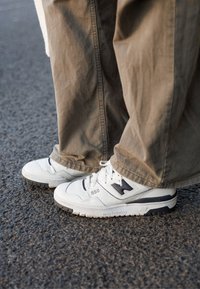 Zapatillas de cuero blancas con acentos grises y una suela texturizada, que presentan un destacado logo "N" y el detalle "550" en el lateral.