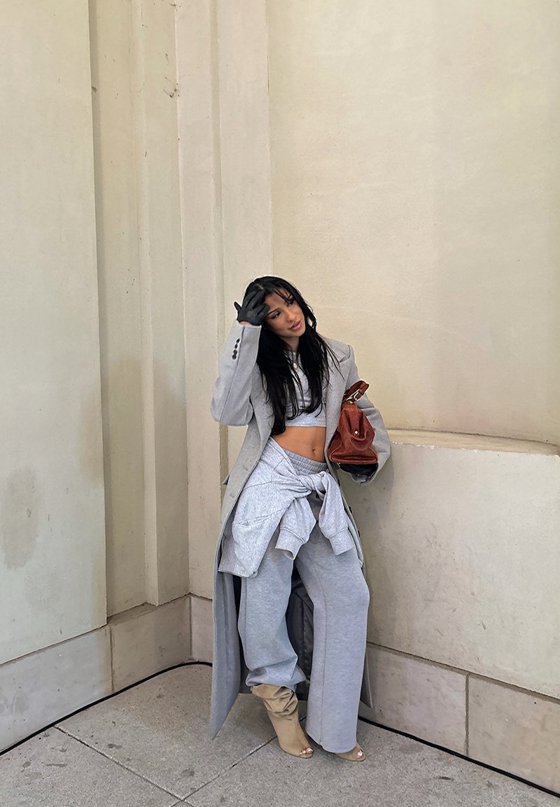 Blazer grigio oversize, pantaloni della tuta abbinati legati in vita, guanti e stivaletti beige chiaro alla caviglia, con una borsa a mano marrone.