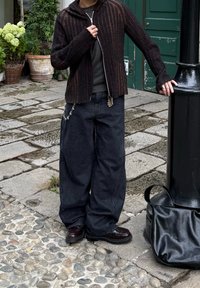Felpa nera a costine con zip, t-shirt grigio scuro, jeans neri oversize, scarpe nere lucide, accento di catena in argento e borsa nera in pelle.