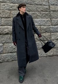 Lange grijze wollen jas met een dubbelgeknoopt ontwerp, zwarte geribbelde kraag, gecombineerd met een zwarte coltrui, grijze broek en groene plateauzolen.