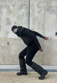 Person wearing a black puffer vest over a ribbed black sweater and relaxed-fit black jeans, paired with slouchy black boots and reflective sunglasses.