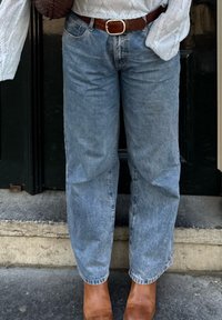Lyseblå denimjeans med en løs pasform, opslået ved anklerne, parret med brune læderankelstøvler og et brunt bælte. Tekstureret hvid sweater synlig.