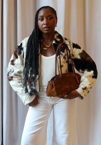 Faux fur jacket featuring a black and brown spotted design, teamed with a white tank top, white wide-leg trousers, and a brown suede handbag.