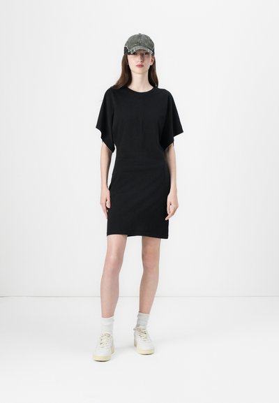 Vestido de algodón negro con mangas cortas, silueta ajustada y escote redondeado. Llevado con una gorra gris y zapatillas blancas.