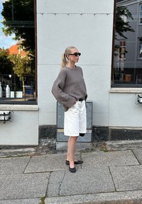 Γκρίζα, υφασμένη υπερμεγέθη ζακέτα, λευκά σορτς, μαύρη ζώνη και παπούτσια με πουά. Στηρίζεται σε ένα ανοιχτό γκρι τοίχο, φοράει γυαλιά ηλίου.